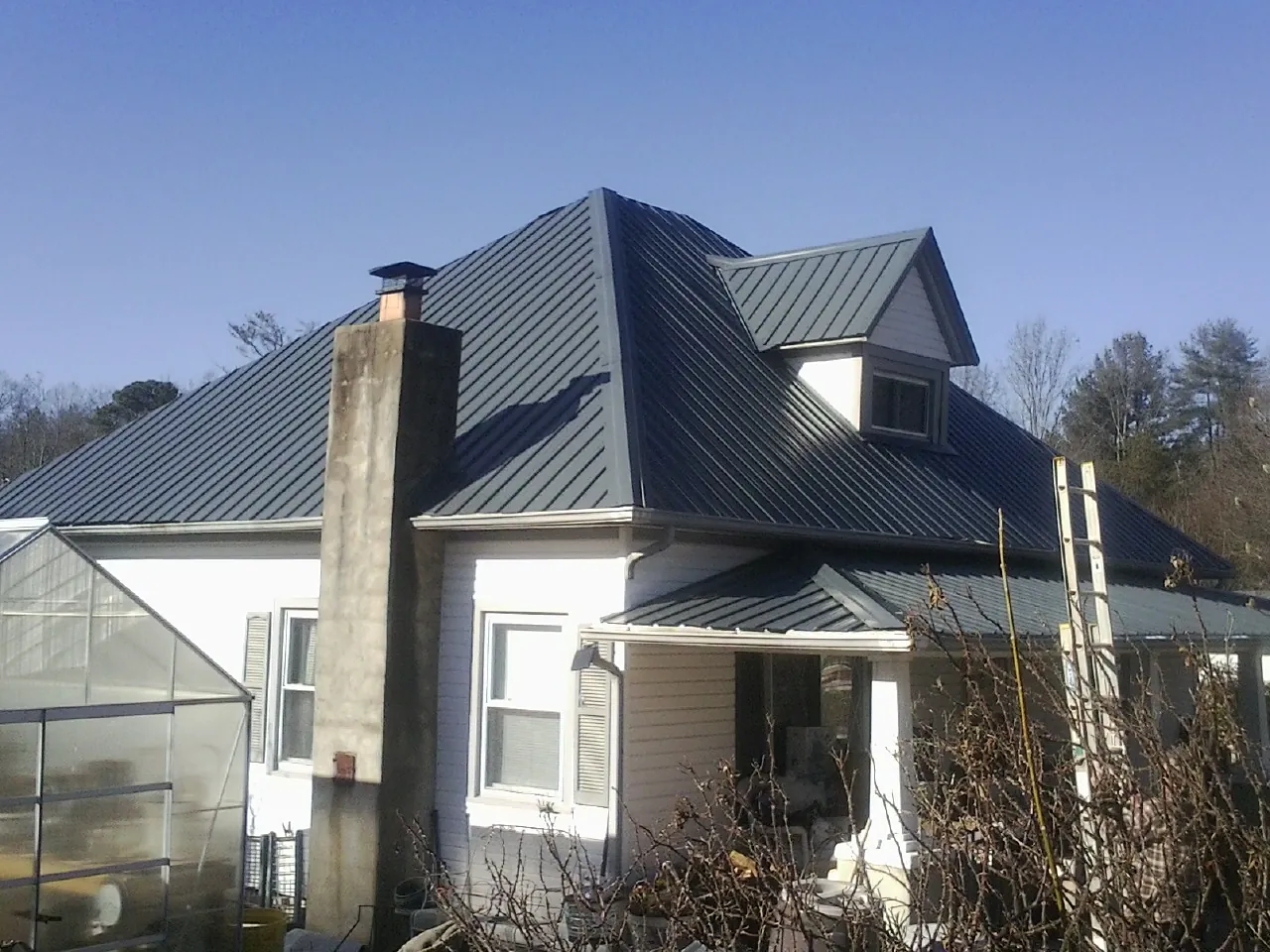 Dark blue standing seam metal roof on a white farmhouse with dormer — Slate & Tile Roof Repair by Roofing Brothers in Thorp