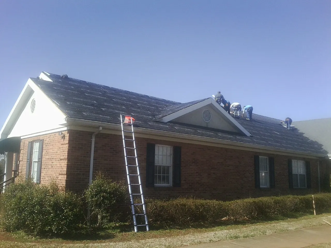 Crew tearing shingles off a brick ranch roof with a ladder set — Emergency Roof Repair work by our crew in Thorp
