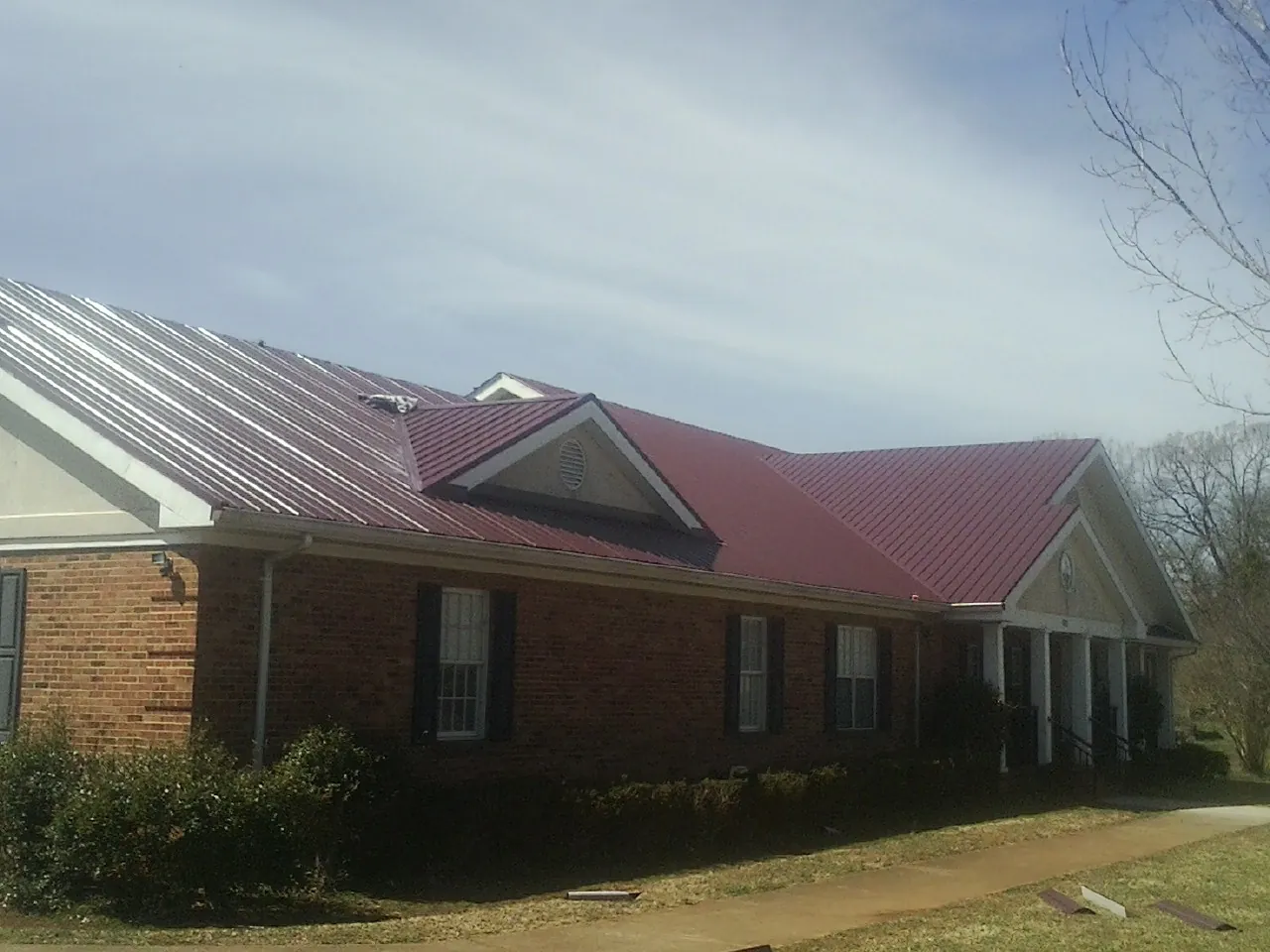 Red metal roof with gabled entries on a long brick building, from a Hail Damage Roof Repair job in Thorp