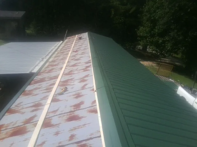 Old rusted panels beside newly installed green metal roofing — Wind Damage Roof Repair by Roofing Brothers in Thorp