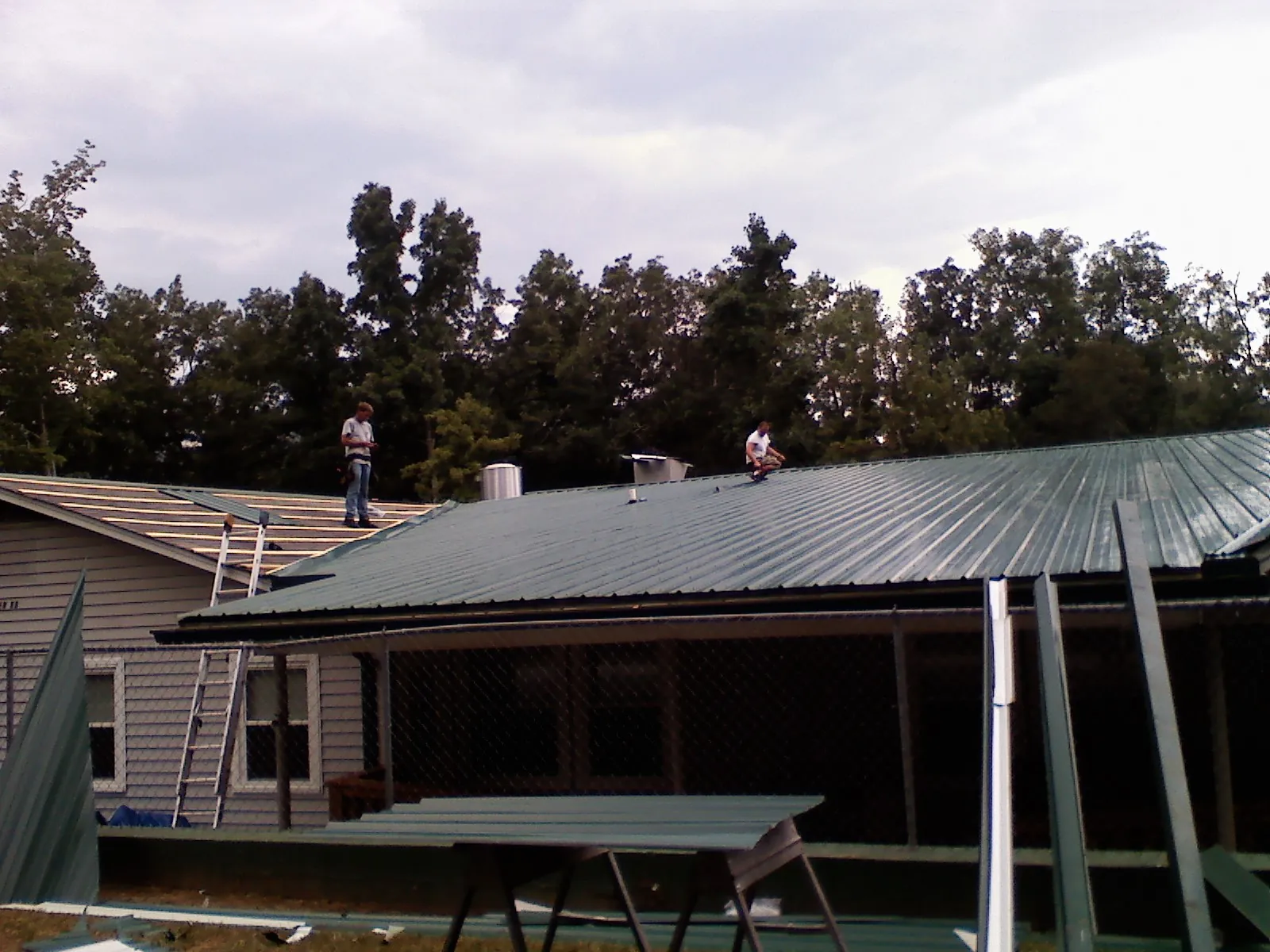Two roofers installing green metal panels above a covered porch in Thorp