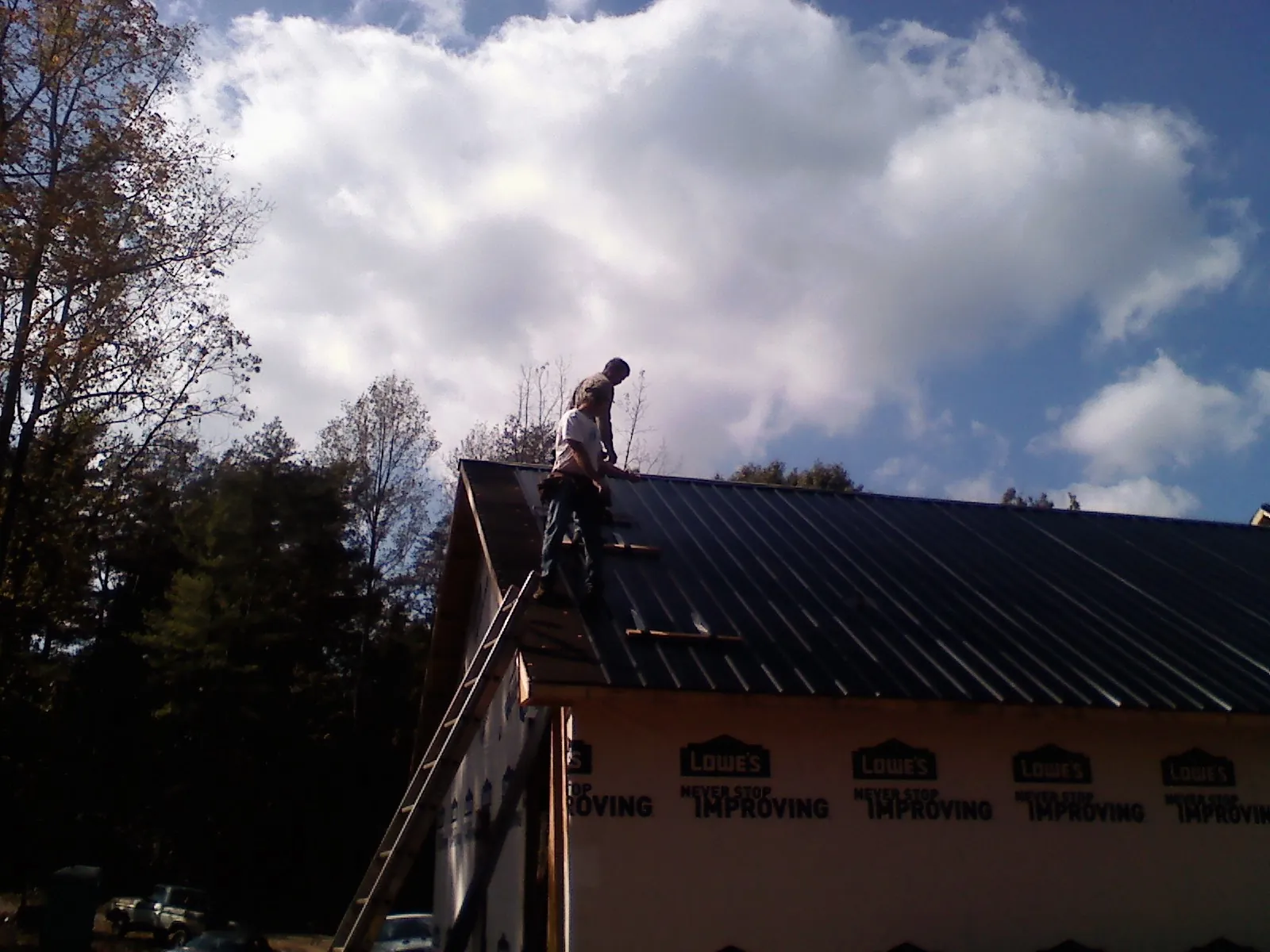 Roofer fastening dark metal panels high against a cloudy sky, from a Roof Inspection job in Thorp
