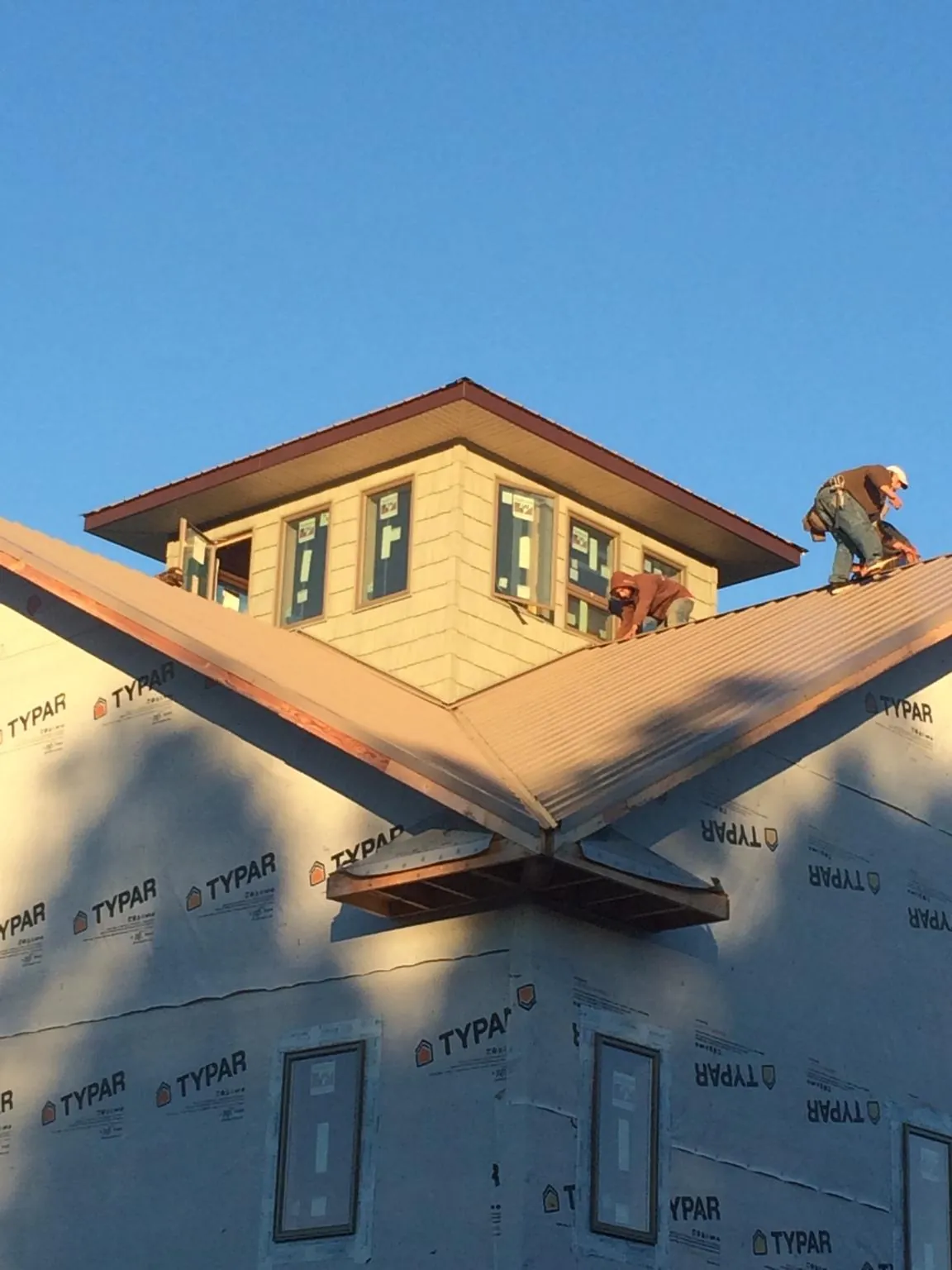 Roofers working around a rooftop cupola on a new metal roof at sunset — Roof Waterproofing in Thorp by Roofing Brothers
